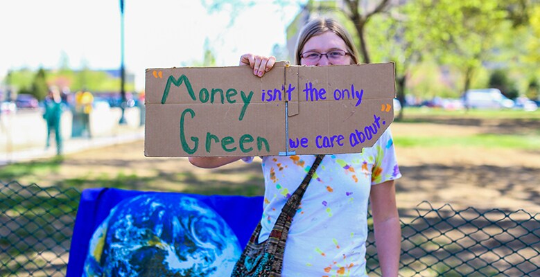 someone holding sign that says Money isn't the only Green we care about