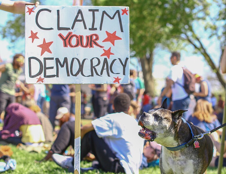 Crowd with someone holding a sign that says Claim your Democracy