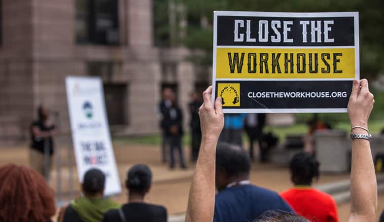 Person holds up a sign that says "Close The Workhouse"